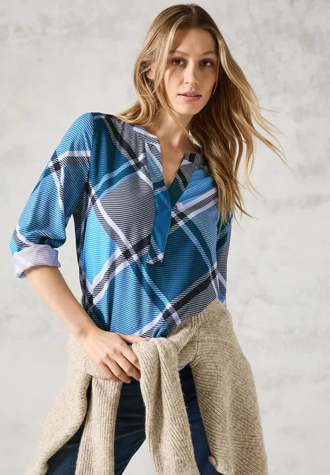 Frau mit blau karierter Bluse und beigem Pullover um die Hüfte.